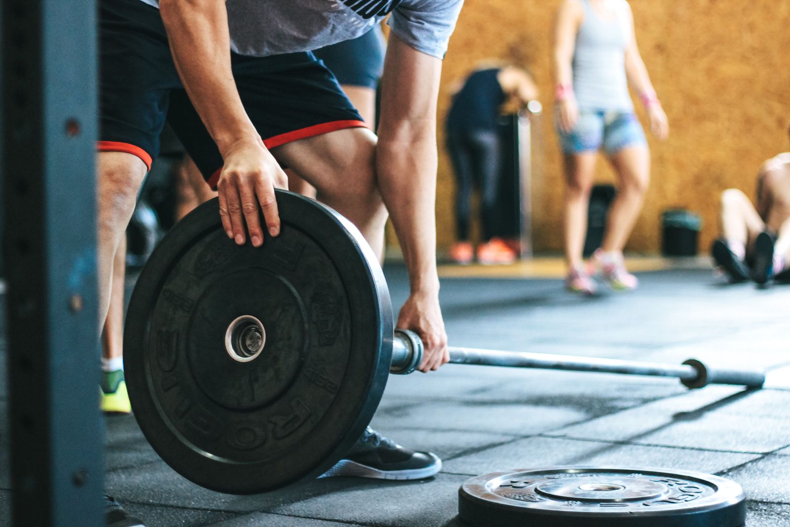 Athlete sliding a black bumper plate onto a barbell on a rubber gym floor