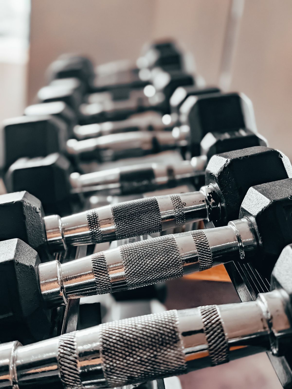 Row of hex dumbbells with knurled chrome handles lined up on a rack