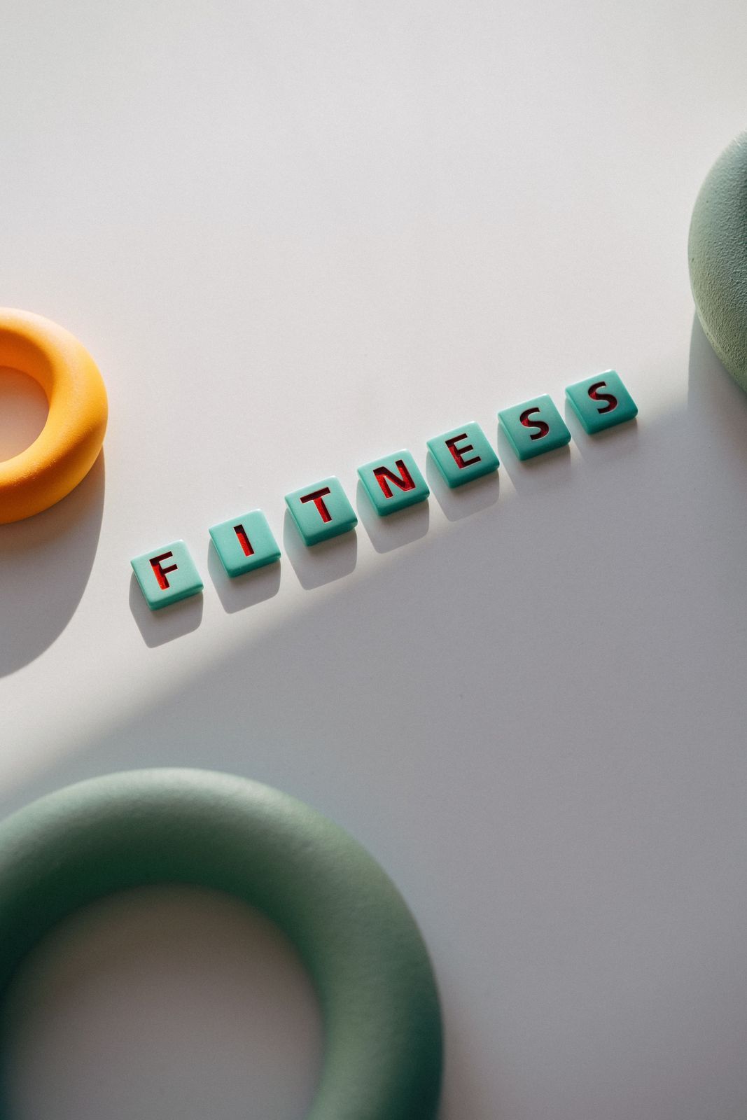 Turquoise letter tiles spelling the word fitness next to soft rubber training rings