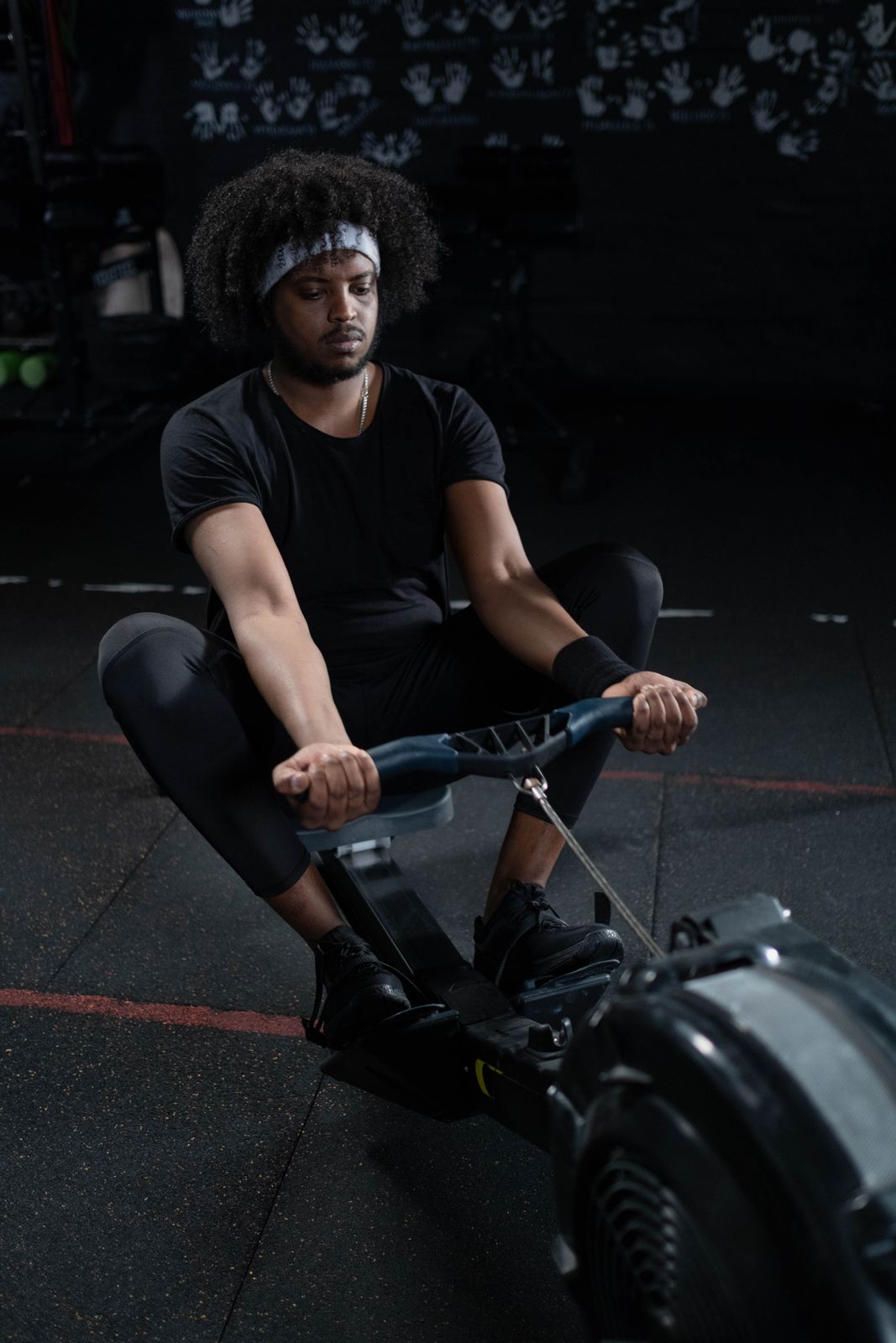 Man in a headband pulling the handle of an indoor rowing machine in a dark gym